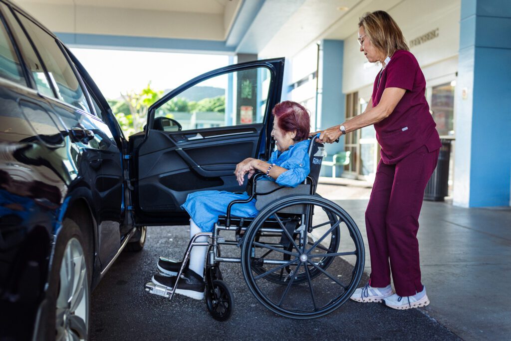 Caregiver pushing elderly woman in wheelchair to car